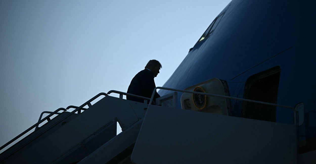 In silhouette against the early morning sky, President Trump at the top of the stairs prepares to board Air Force One.