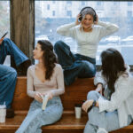 A mixed-raced group of young women sit on a bench and ledge interacting.