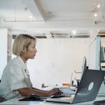 A woman working intently on a computer in a bright, modern office setting.